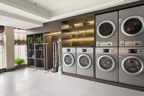 A laundry facility with multiple washing machines and dryers, a metal drying rack, and shelves with plants. - Great Wall Hotel (Shaoyang)