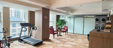 A hotel room with a treadmill, exercise bike, and a large window with a city view.