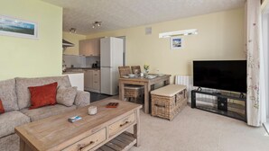 A living room with a sofa, coffee table, TV, dining table, and kitchen in the background. - Harbour Reach - Close to Beach, Parking (Saundersfoot)
