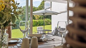 An outdoor dining area with a table set for two, a large umbrella, and a view of a garden and house in the background. - Harbour Reach - Close to Beach, Parking (Saundersfoot)