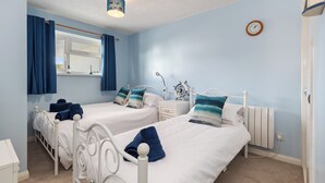 A bedroom with two beds, a window with curtains, a clock on the wall, and a radiator. - Harbour Reach - Close to Beach, Parking (Saundersfoot)