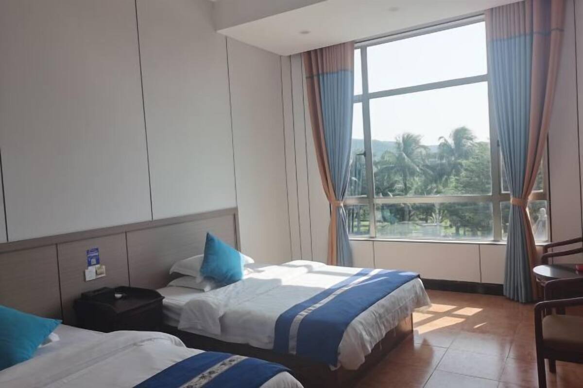 Ein Hotelzimmer mit zwei Betten, einem Schreibtisch und einem großen Fenster mit Vorhängen.