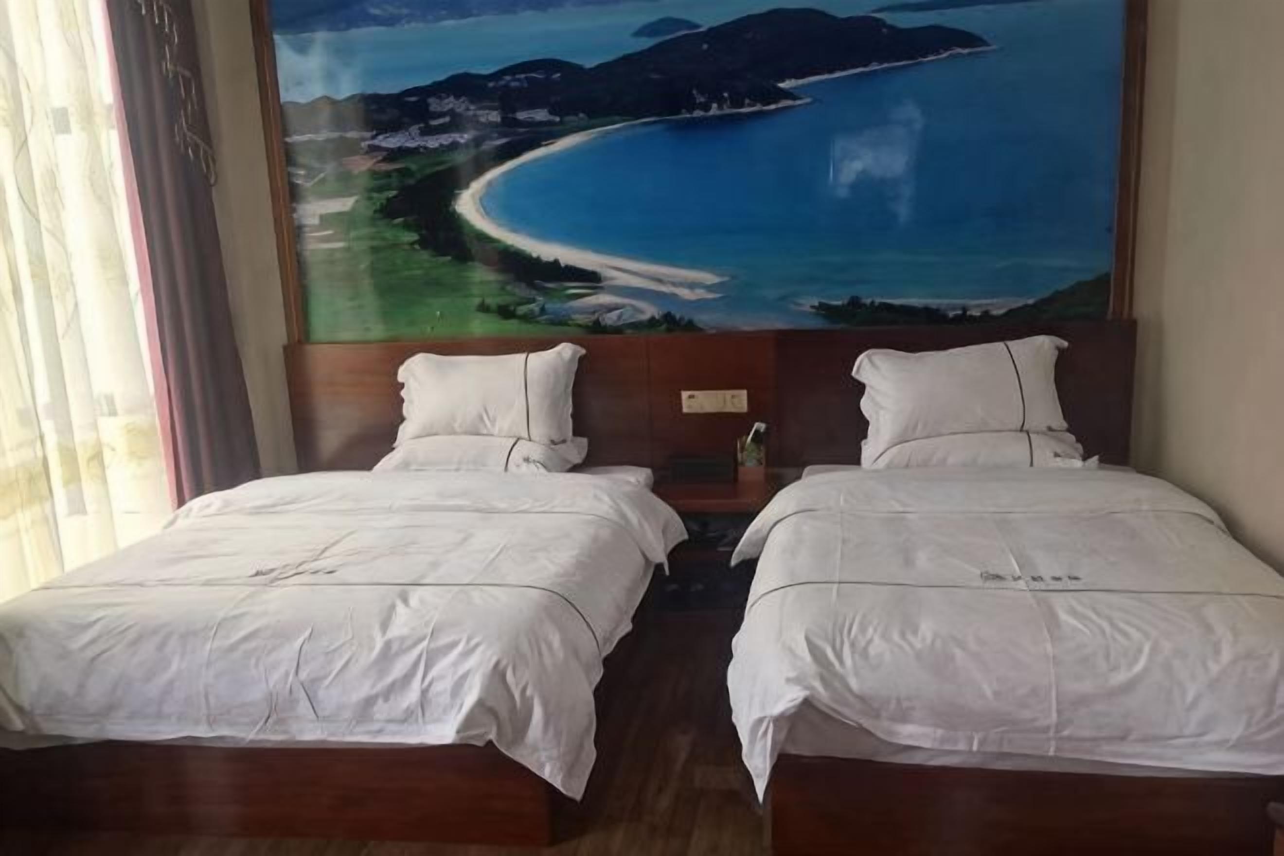 Deux lits avec du linge de lit blanc, un grand tableau représentant une plage et des montagnes, et une tête de lit en bois.