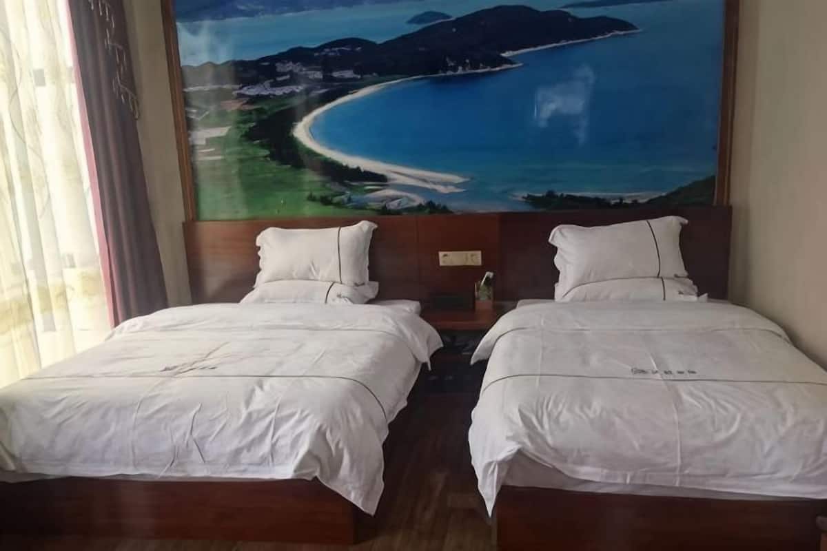 Zwei Betten mit weißer Bettwäsche, ein großes Gemälde von Strand und Bergen sowie ein hölzerner Kopfteil.