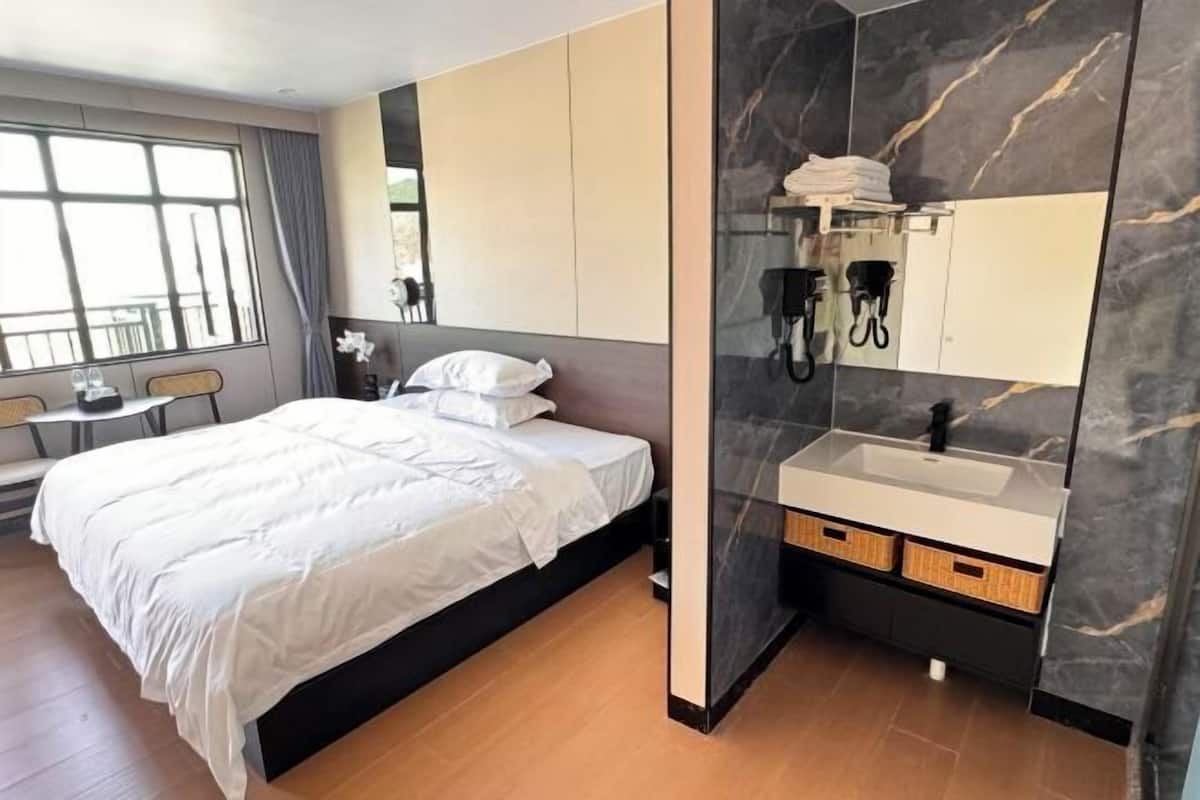 Ein modernes Hotelzimmer mit einem großen Bett, einem integrierten Schminktisch mit Spiegel und Blick ins Freie durch ein Fenster.