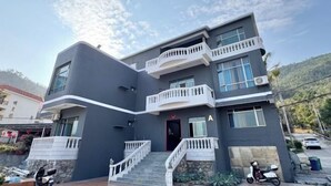 A modern multi-story building with a dark facade, multiple balconies, and a central entrance with a red door.