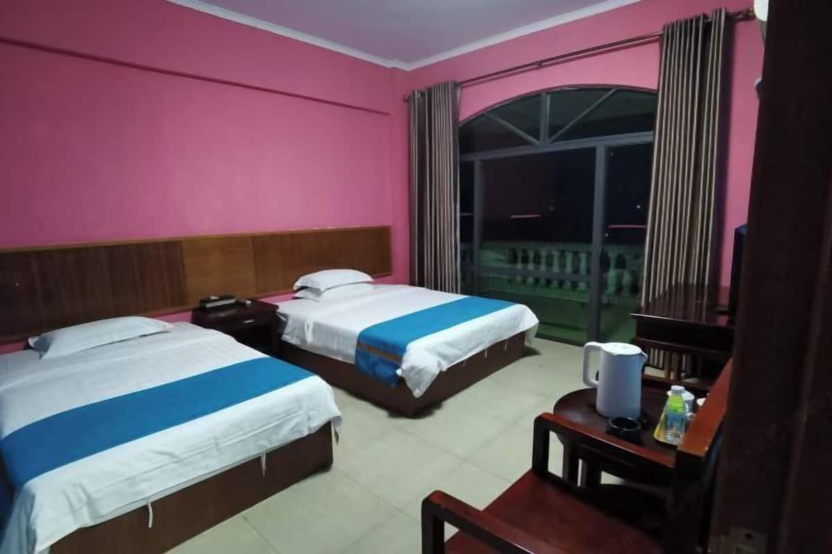 Ein Hotelzimmer mit zwei Betten, einem Holz-Kopfteil, einem kleinen Tisch mit Wasserkocher und einem Fenster mit Vorhängen.