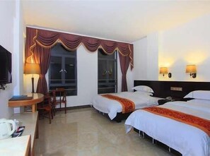 Habitación de hotel con dos camas, un escritorio, una silla, un televisor y dos lámparas de pared.