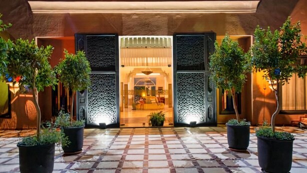 L’entrée d’un hôtel, avec un sol à carreaux, des plantes en pot et des panneaux décoratifs.