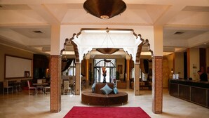 Un hall d’entrée spacieux avec un tapis rouge, un espace salon circulaire agrémenté de coussins et un comptoir d’accueil.