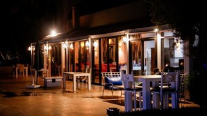 Un espace extérieur aménagé avec des tables et des chaises, une partie couverte avec des murs en verre et un éclairage soigné.