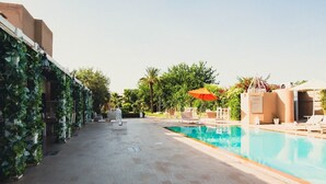 Un espace piscine avec une piscine à l’eau d’un bleu limpide, des chaises longues et un parasol orange.
