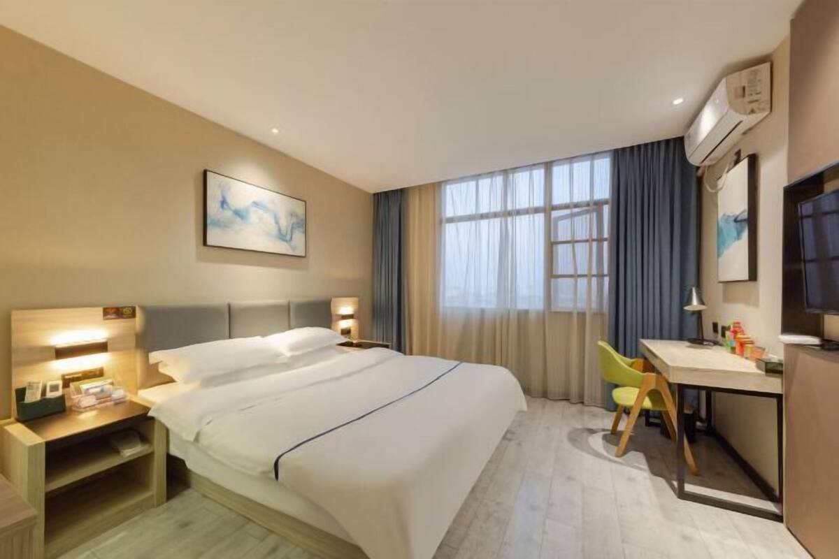 Une chambre d’hôtel comprenant un lit, des tables de chevet, un bureau avec une chaise et une grande fenêtre avec des rideaux.