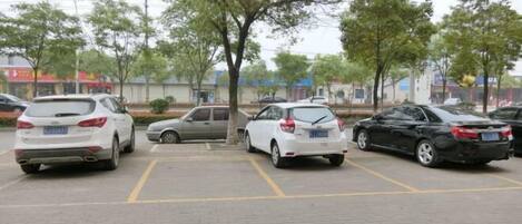 A parking lot with several cars parked, trees, and buildings in the background.