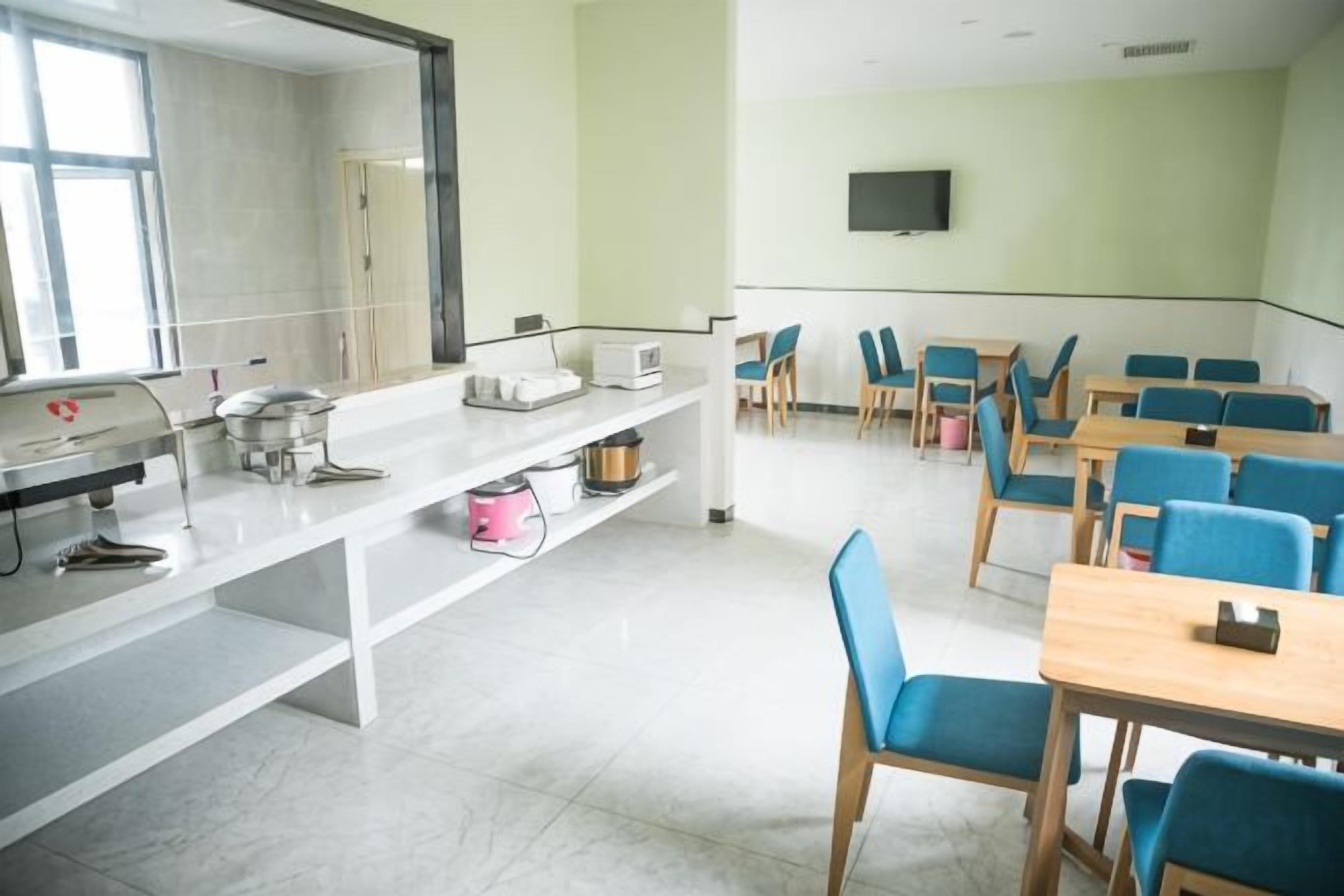 A classroom with white desks, blue chairs, a whiteboard, and a television on the wall.
