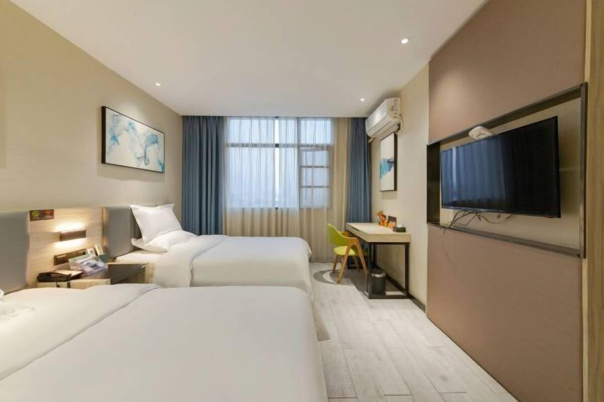 Une chambre d’hôtel avec deux lits, un bureau, une télévision et une fenêtre avec des rideaux.