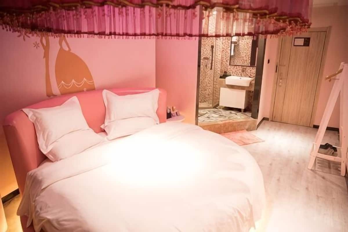 Une chambre à coucher comprenant un lit, une table de chevet, un miroir et une porte donnant accès à une salle de bain.