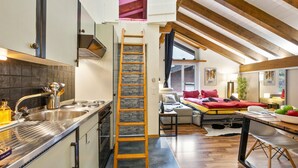 A modern kitchen with a wooden ladder, a dining area with a table and chairs, and a loft bedroom with a red bedspread. - Haus Bodmen B Apartment B 43 by Interhome (Zermatt)