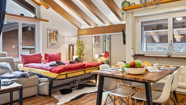 A cozy room with a bed, a dining table with chairs, a sofa, and a window with a view. - Haus Bodmen B Apartment B 43 by Interhome (Zermatt)
