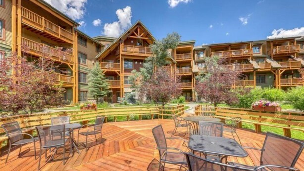 A wooden deck with outdoor seating and a view of a multi-story building with balconies. - Tenderfoot Lodge 2 Bedroom at the Mountain House Base (Keystone)