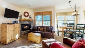 A cozy living room with a fireplace, a sofa, a coffee table, and a dining area with chairs and a table. - Tenderfoot Lodge 2 Bedroom at the Mountain House Base (Keystone)