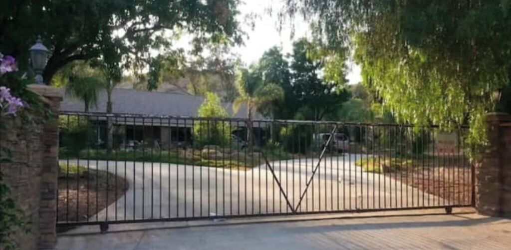 A gated driveway leading to a building with a brick wall and a metal gate.