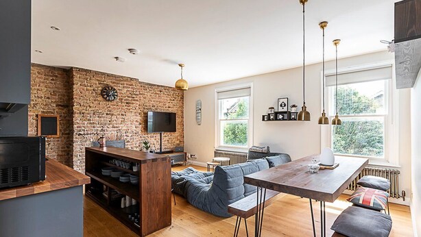 A modern kitchen with a brick wall, wooden flooring, and a dining area with a table and benches.