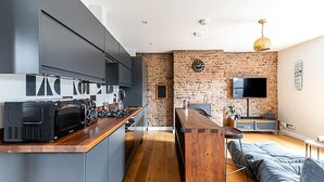A modern kitchen with a brick wall, a large TV, and a wooden dining table.