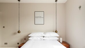 A bedroom with a bed, white pillows, a bedside table with a lamp, and a wall-mounted light fixture.