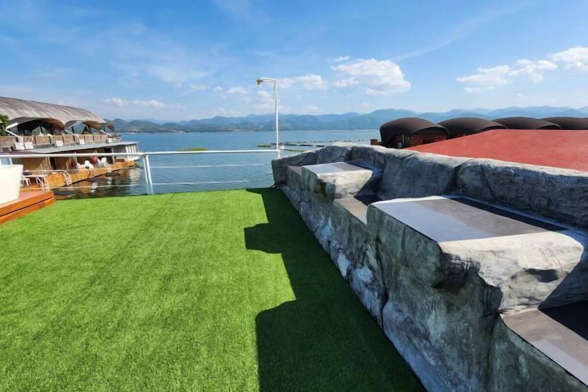 A boat with a covered deck and a grassy area with stone steps leading to a water feature.