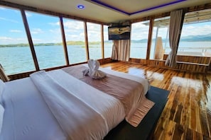 Une chambre dotée d’un lit, de grandes fenêtres, d’un téléviseur à écran plat et d’un plancher en bois.