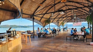 An outdoor wooden deck with tables and chairs, overlooking a body of water and hills. - Banrai WanWan Resort (Si Sawat)