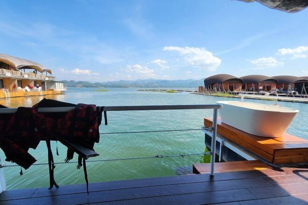 A floating hotel with overwater bungalows, a dining area with a table and chairs, and a boat docked nearby.