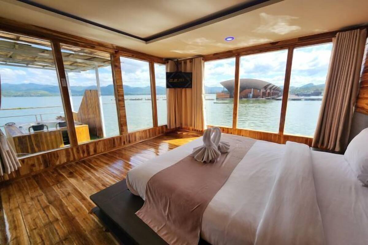 A spacious room with a large bed, wooden flooring, and a view of a body of water and a distinctive building.