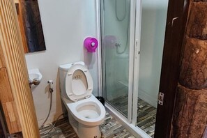 A bathroom with a toilet, a shower with a glass door, and a wooden floor. - Banrai WanWan Resort (Si Sawat)