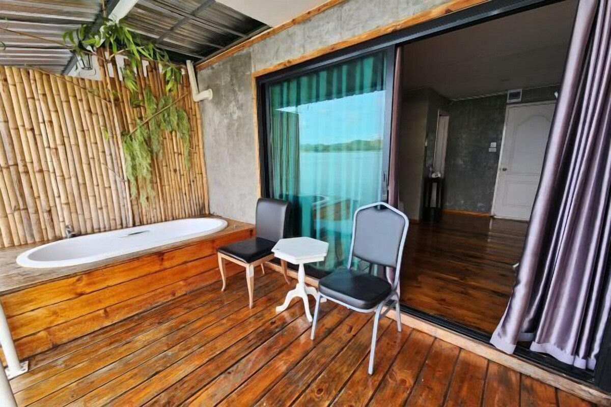 A wooden deck with a bathtub, two chairs, and a table.