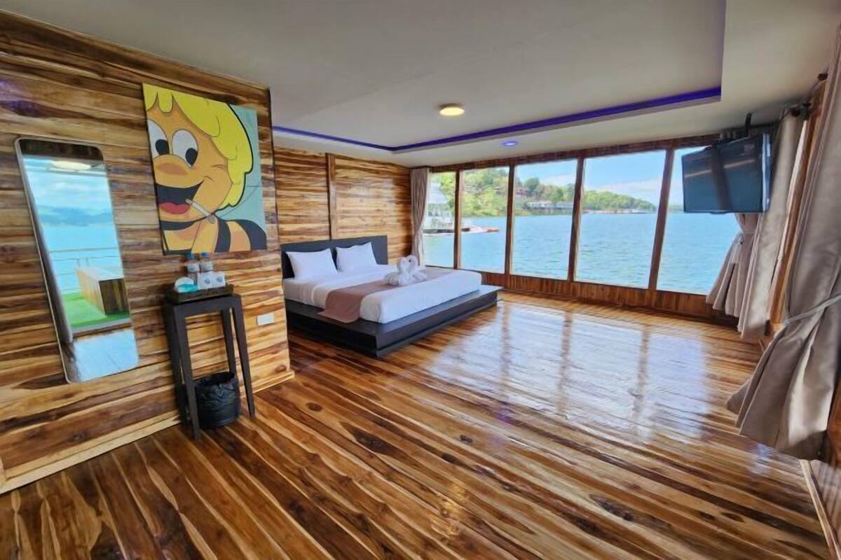 A room with a bed, a TV, a large window, and a wooden floor.