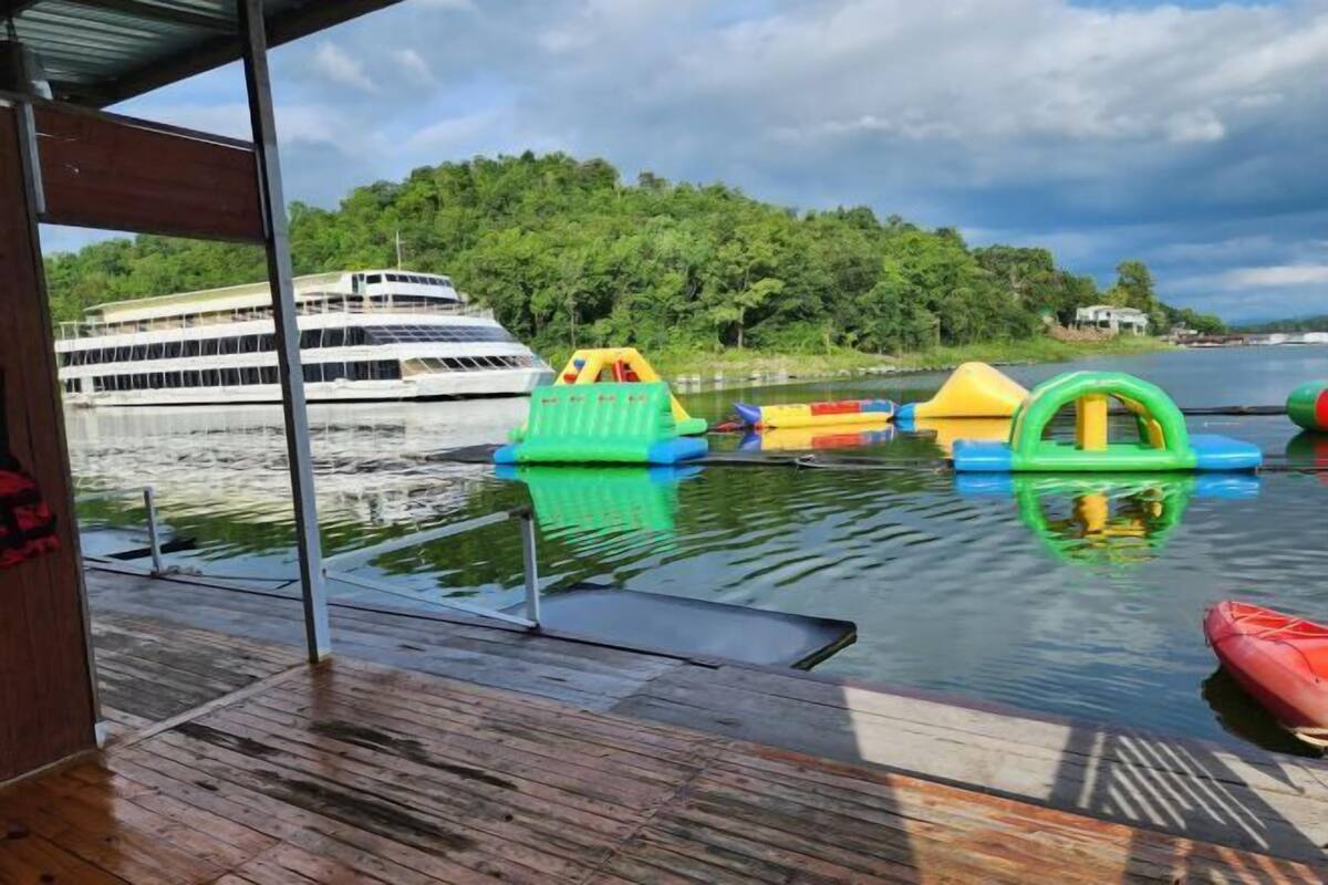 A wooden deck with colorful inflatable toys and a red kayak. A large cruise ship is visible in the background.
