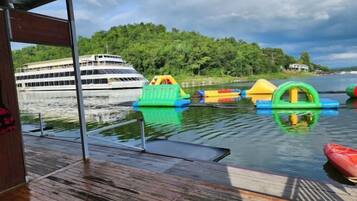 Una cubierta de madera con juguetes inflables de colores y un kayak rojo. Se ve un gran crucero al fondo.