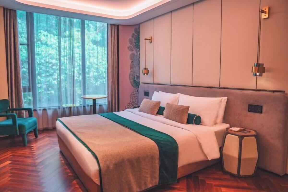 Ein Hotelzimmer mit einem großen Bett, einem kleinen runden Tisch, einem Sessel und Blick ins Freie durch das Fenster.