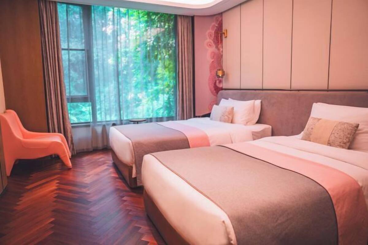 Ein Hotelzimmer mit zwei Betten, einem Fenster mit Vorhängen, einem Holzboden und einem rosa Sessel.