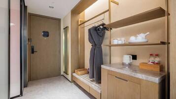 A compact hotel room with a wooden wardrobe, a small kitchenette, and a shower area.