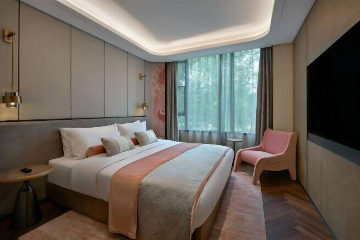 Ein modernes Hotelzimmer mit einem großen Bett, einem kleinen Nachttisch, einem Sessel und einem Fernseher.