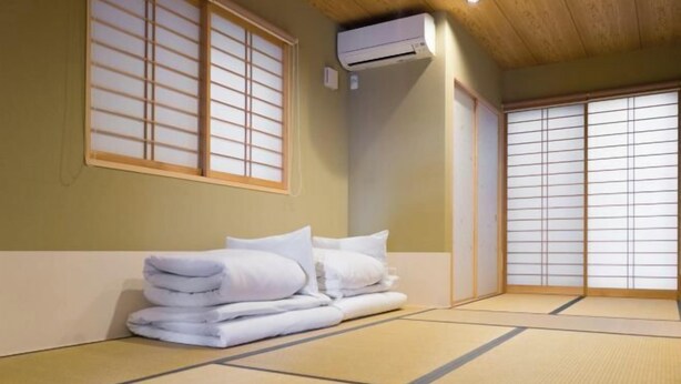 Une pièce de style japonais traditionnel, avec un sol recouvert de tatamis, une pile de serviettes blanches et des portes coulissantes en papier de riz (shoji).