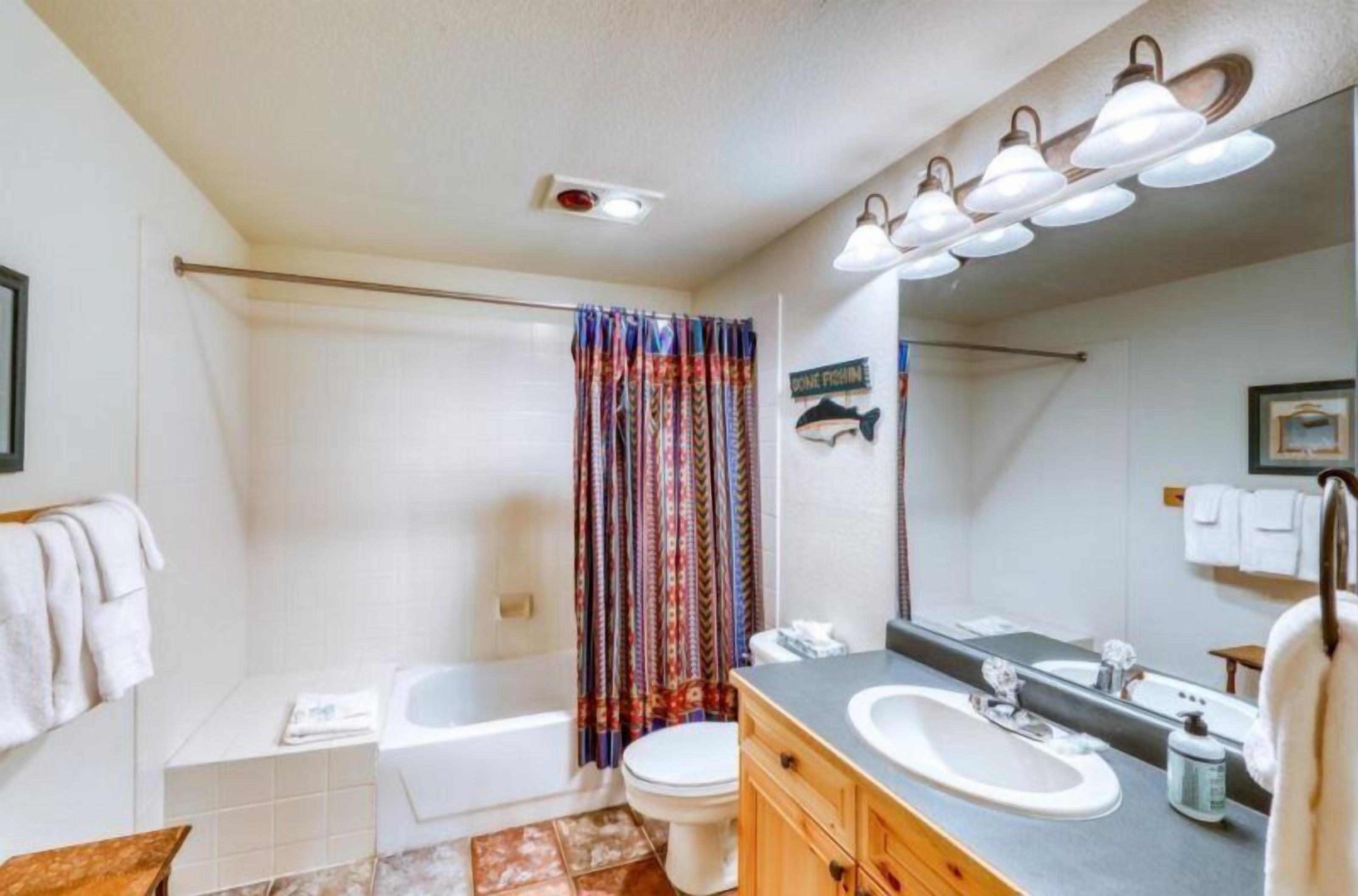 Un baño con bañera, inodoro y lavamanos. Hay una cortina de ducha con un estampado colorido.