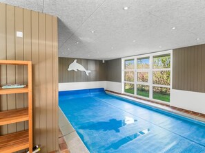 Una piscina interior con un mural de delfines, estanterías de madera y ventanas amplias.