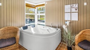 Un cuarto de spa con un jacuzzi grande, sillas de mimbre y vistas al exterior.