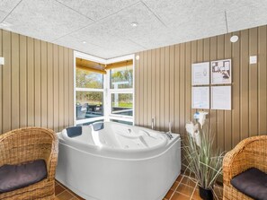 Uma sala de spa com uma banheira de hidromassagem grande, cadeiras de vime e vista para o exterior.