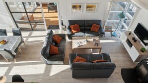 Un salón moderno con dos sofás, una mesa de centro y un televisor. Se ven ventanas grandes y un balcón.