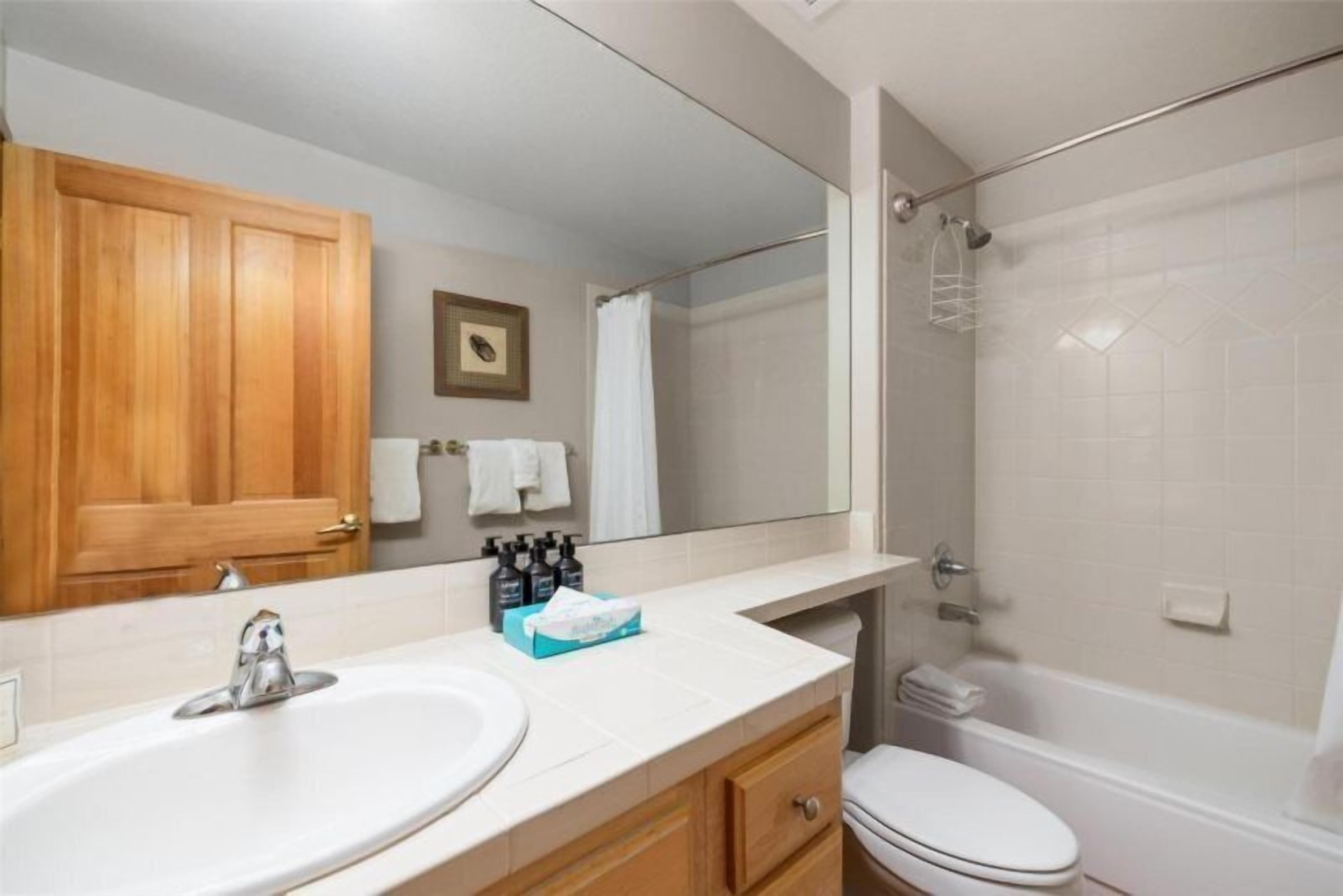 A bathroom with a wooden vanity, a sink, a mirror, a toilet, and a shower.